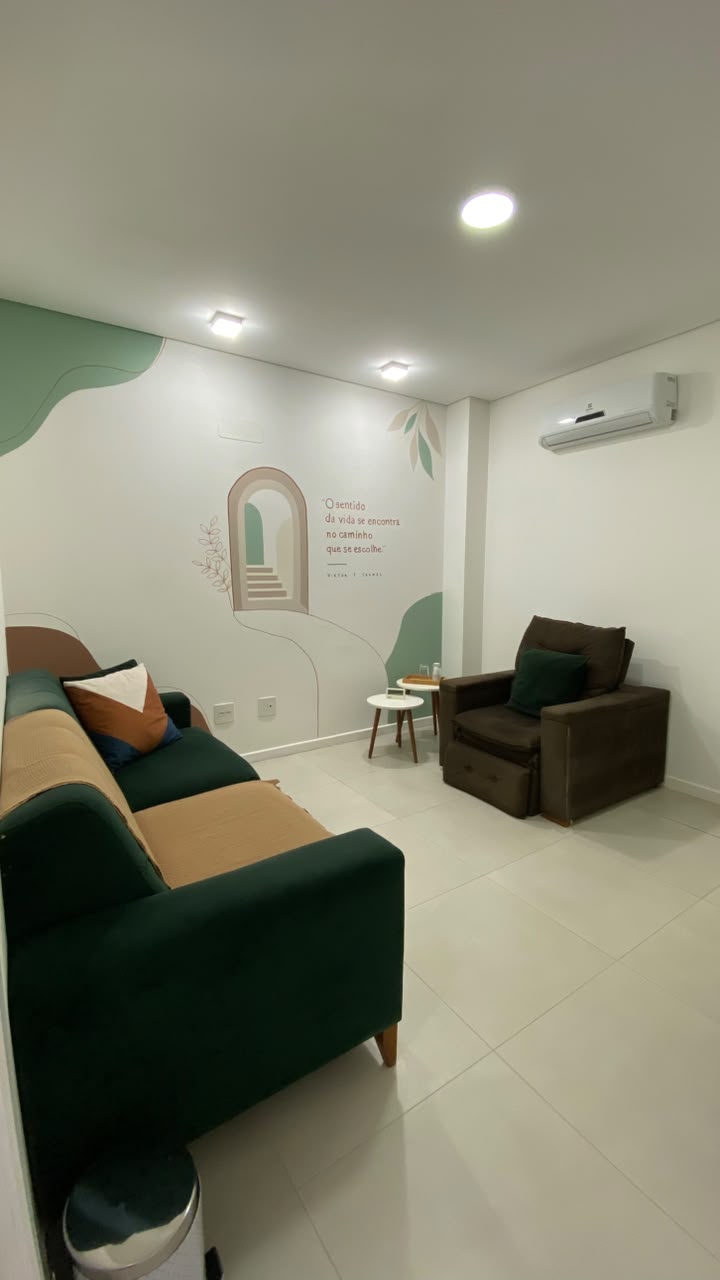 Consultório de Priscilla Vogt em Coqueiros, com sofá verde, poltrona e parede com pintura decorativa