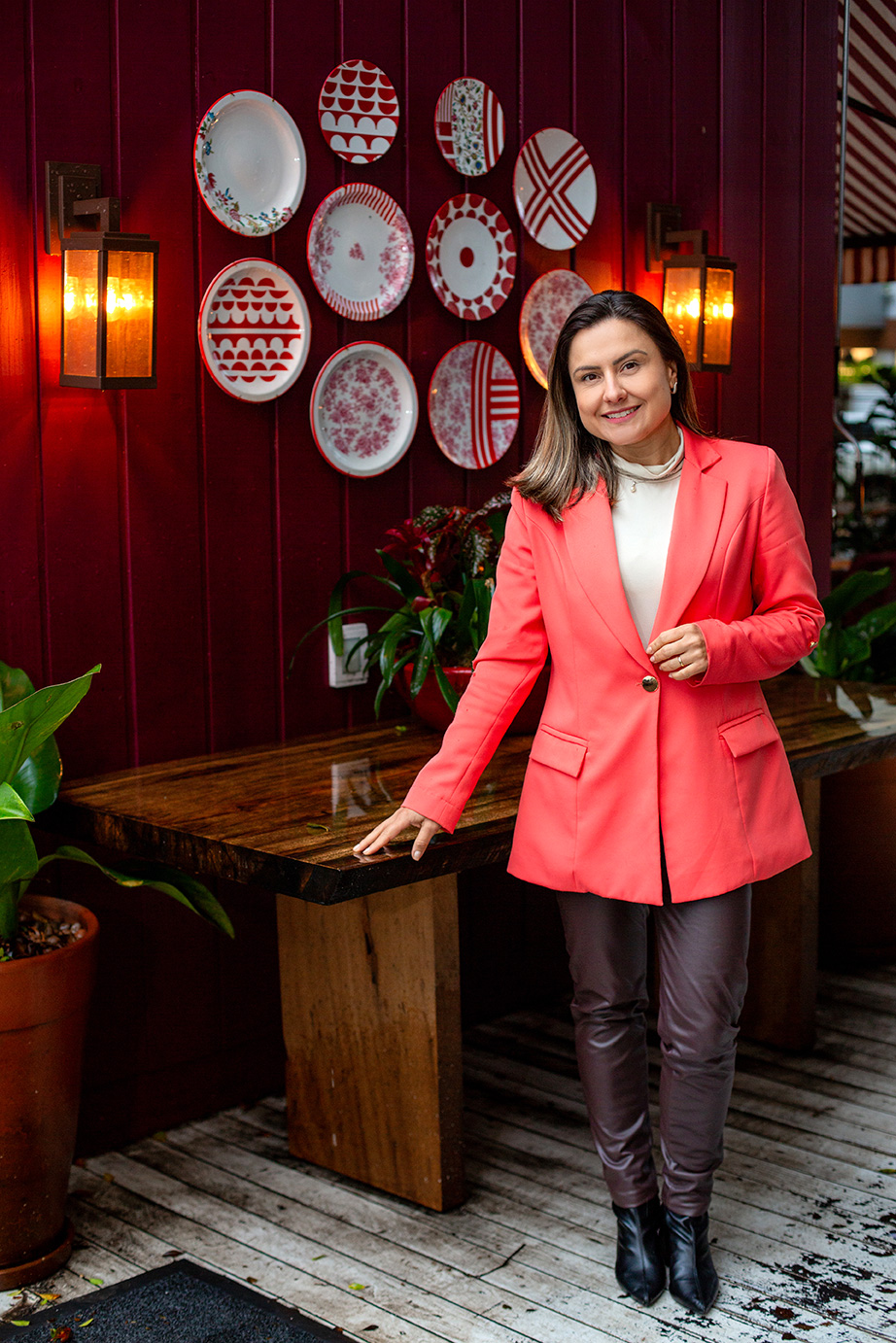 Psicóloga Priscilla Vogt de corpo inteiro, com blazer coral, diante de uma parede decorada