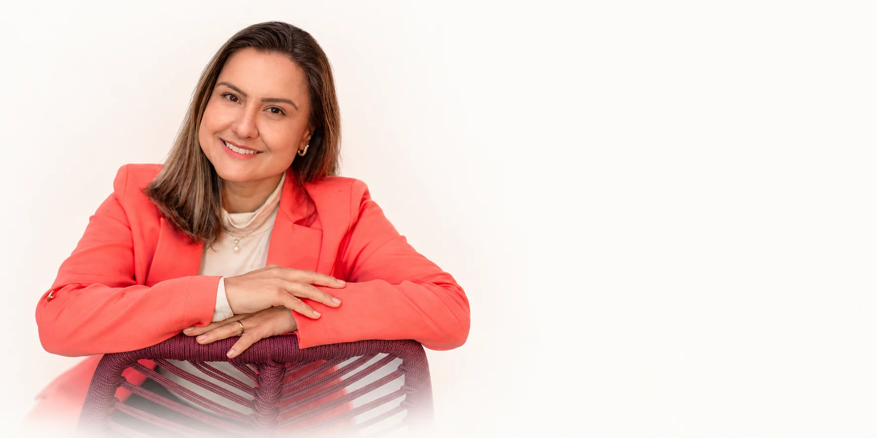 Psicóloga Priscilla Vogt com blazer coral, sorrindo em um fundo claro