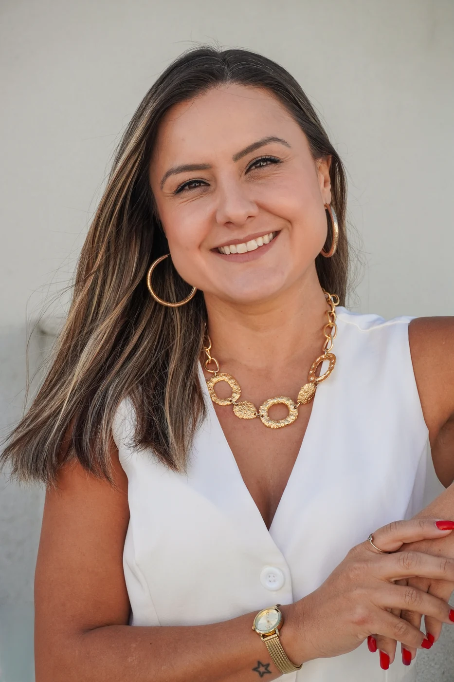 Priscilla Vogt sorrindo, com blusa branca e colar dourado