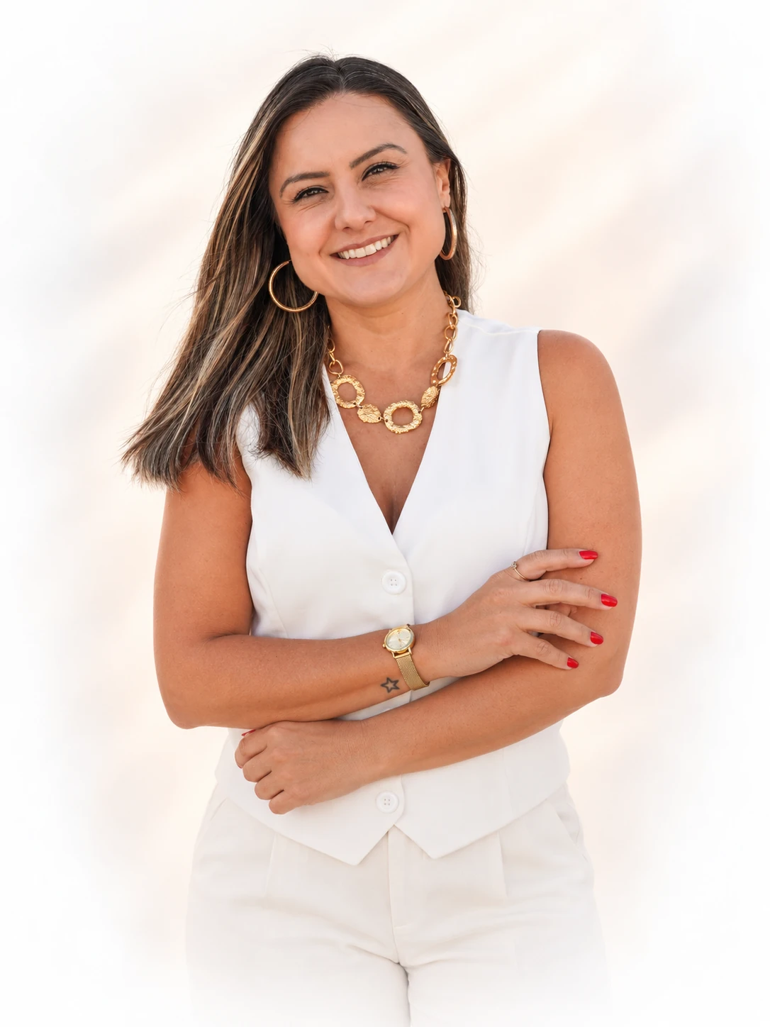 Priscilla Vogt sorrindo, com roupa branca e braços cruzados, em fundo claro